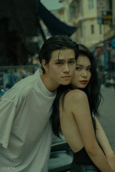 two people standing next to each other in front of a car on a city street