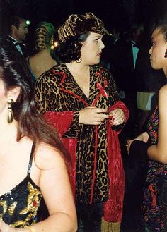 two women dressed in animal print clothing talking to each other at a formal event with others looking on