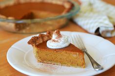 a slice of pumpkin pie on a plate with a fork and bowl in the background