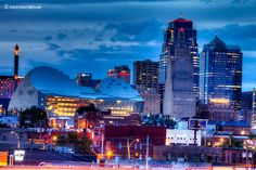 the city skyline is lit up at night, with buildings in the foreground and lights on