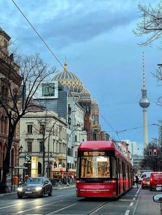 a red bus driving down a street next to tall buildings and traffic lights on a cloudy day