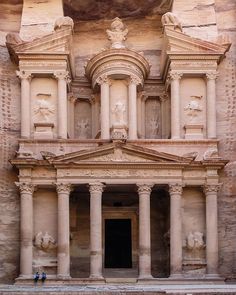 two people standing in front of an ancient building with statues on the walls and columns