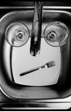 a black and white photo of two wine glasses in a sink with a knife and fork sticking out of it