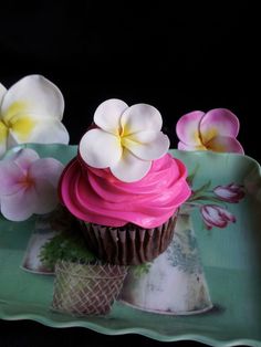 a cupcake with pink icing and white flowers on it sitting on a plate