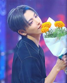 a young man holding a bouquet of flowers in front of his face and looking up at the sky