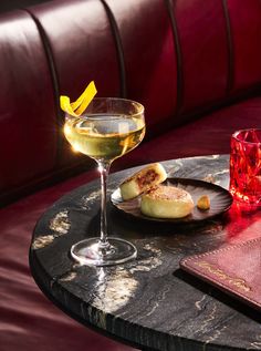 a glass of wine and some food on a table with a red leather chair in the background