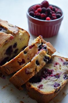 blueberry bread cut into slices on a cutting board next to a bowl of berries