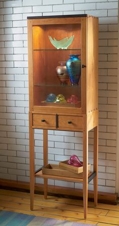 a wooden cabinet with glass doors and drawers on the bottom shelf in front of a brick wall