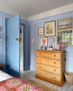 a bedroom with blue walls and pictures on the wall next to a wooden chest of drawers