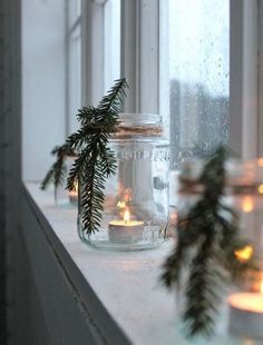 candles are sitting on a window sill in front of the windowsill and evergreen branches