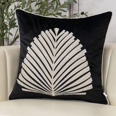 a black and white pillow sitting on top of a couch next to a potted plant