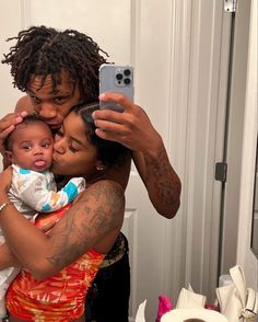 a woman holding a baby and taking a selfie with her cell phone in front of the mirror