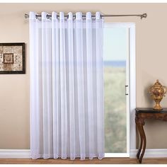 a white curtain hanging on the side of a window next to a table with a vase