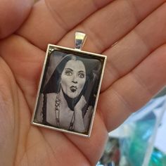 This 1" x 1.35" rectangle pendant features Goth Mom and TV icon Caroline Jones as Morticia Addams in the original 1960s Addams Family TV series. Comes with your choice of 24" silver chain, 30" silver ball chain, or silver keychain. Creepy, Kooky, Mysterious, and Spooky. Goth Mom, Caroline Jones, Family Tv Series, Lily Munster, Julie Newmar, Young Frankenstein, Morticia Addams, Family Tv, Tv Icon