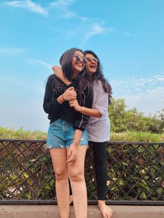 two young women standing next to each other on a bridge with blue sky in the background