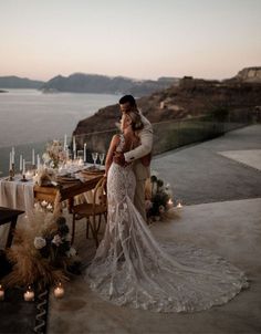 a bride and groom standing in front of a table with candles on it, overlooking the ocean