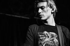 black and white photograph of a young man holding a guitar in his right hand while wearing a t - shirt with an image of a snake on it