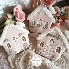 three small pink houses sitting on top of a white lace tablecloth next to flowers