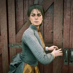 a woman standing in front of a wooden door wearing a green and yellow dress with her hands on her hips