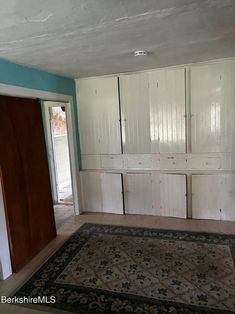 an empty room with white cupboards and carpet in the middle, next to a doorway