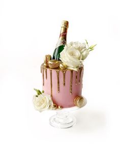 a pink cake with white roses and champagne on top, sitting next to a wine bottle