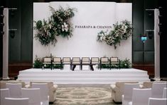 an empty stage set up for a wedding ceremony with chairs and flowers on the wall