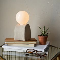 a glass table topped with books and a light on top of each other next to a potted plant