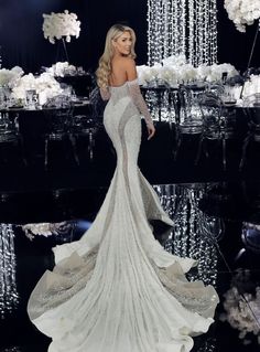 a woman in a white dress standing next to a table with flowers and chandeliers