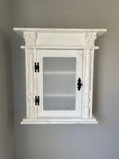 an old white cabinet with glass doors on the top and bottom is against a gray wall