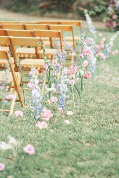 rows of wooden chairs sitting on top of a grass covered field next to pink and blue flowers