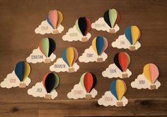 colorful hot air balloons with name tags attached to them on a wooden table in the shape of clouds