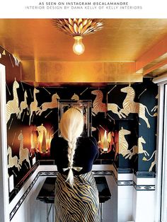 a woman sitting at a desk in front of a wallpapered room with horses on it