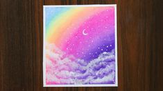 a card with a painting of a rainbow in the sky and stars above it on a wooden surface