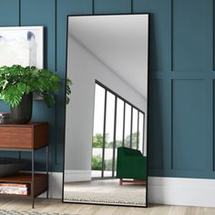 a large mirror sitting on top of a wooden floor next to a table with a plant