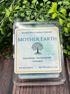 a candle that reads mother earth surrounded by greenery on a wooden table with the words, grounding nourishment guidance