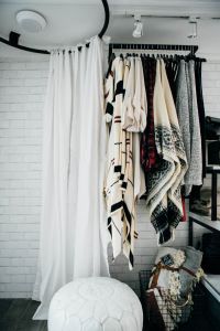 a white bench sitting under a window next to a bunch of clothes hanging on a rack