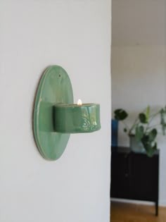 a green light fixture mounted to the side of a wall next to a potted plant