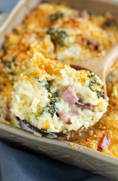 a casserole dish with broccoli, ham and cheese in it is being lifted by a wooden spoon