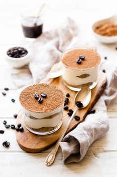 two desserts are sitting on a wooden board with spoons and coffee beans around them