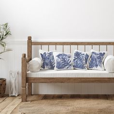 a wooden bench with blue and white pillows on it next to a potted plant