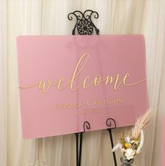 a pink welcome sign sitting on top of a table next to two vases filled with flowers