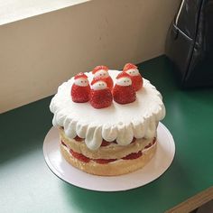 a cake with strawberries on top sitting on a green table next to a black purse