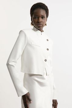 Increase The Formality In Our Cropped Jacket, Which Features A Full-Coverage High Neckline To Protect From The Elements, As Well As A High Collar And A Slightly Cropped Length. Style It With Tailored Trousers And Pointed Toe Heels For A Statement Occasion Look, Perfect For Cool Days That Require An Elevated Look. Button Detail Luxe Ponte Jersey Cropped Jacket Formal High Neckline And Collar Fitted Silhouette Unique Asymmetric Button Detailing Cropped Length White Button-up Outerwear With Button Cuffs, White Button-up Outerwear With Hidden Closure, Beige Buttoned Cropped Jacket For Work, White Outerwear With Snap Buttons For Work, Beige Cropped Jacket With Buttons For Work, White Snap Button Outerwear For Work, Elegant Button-up Cropped Jacket, White Workwear Outerwear With Button Cuffs, Spring Cream Blazer With Button Cuffs