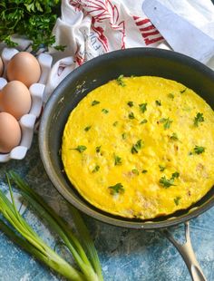 an omelet in a skillet next to eggs and green onions