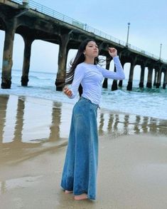 a woman standing on top of a sandy beach next to the ocean with her arms in the air