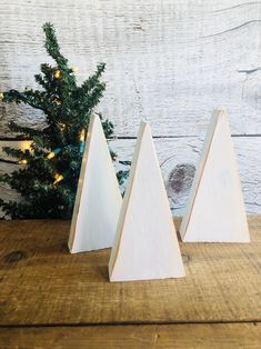 three white wooden christmas trees sitting on top of a wooden table next to a pine tree