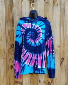 a blue and pink tie - dyed shirt hanging on a wooden wall with a hanger