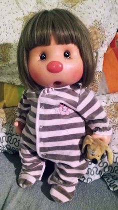 a doll is sitting on the bed with its mouth open and eyes wide open, wearing striped pajamas