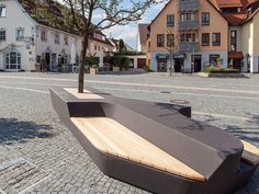 a wooden bench sitting on the side of a road next to tall buildings and trees