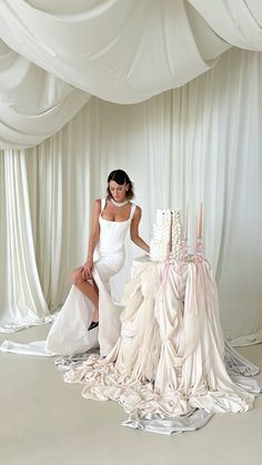 a woman in a white dress sitting next to two wedding gowns on the floor